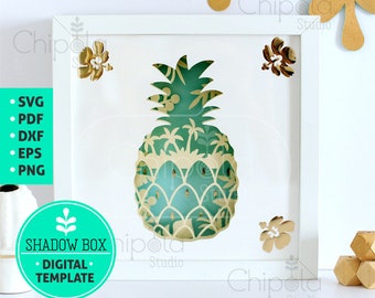May include: A white frame with a green and yellow pineapple shadow box design. The frame is on a white background with gold and blue leaves. The text "SHADOW BOX DIGITAL TEMPLATE" is on a turquoise circle.