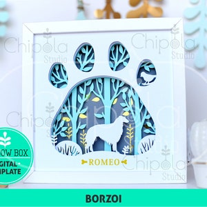 May include: A white shadow box with a blue and green paw print design. Inside the paw print is a forest scene with a white Borzoi dog standing in the center. The dog's name, "ROMEO", is written below the scene.