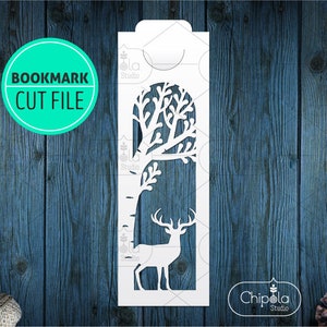 May include: White silhouette cut file of a deer standing in front of a tree with branches. The file is for a bookmark and includes the text "BOOKMARK CUT FILE" and "Chipola Studio".