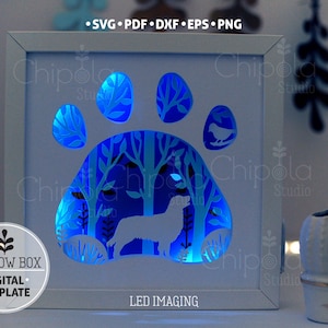 May include: A white shadow box with a paw print design, featuring a dog silhouette and forest scene illuminated by blue LED lights. The design includes a bird and the text "SHADOW BOX DIGITAL TEMPLATE".