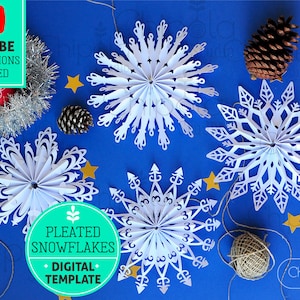 May include: White paper pleated snowflakes in various designs, with gold star accents, and pine cones on a blue background. The image includes text that says "Pleated Snowflakes - Digital Template" and "YouTube Instructions Included".