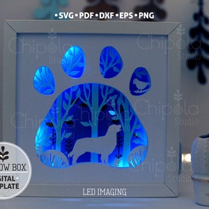 May include: A white shadow box with a blue LED light shining through a cut-out design of a dog paw print with a dog and trees inside. The text "LED IMAGING" is printed below the design. The text "SHADOW BOX &bull; DIGITAL &bull; TEMPLATE" is printed on the left side of the image.