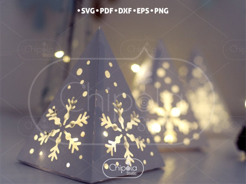 May include: White paper pyramid with a snowflake design and a light inside. The pyramid is decorated with white dots to resemble snow.