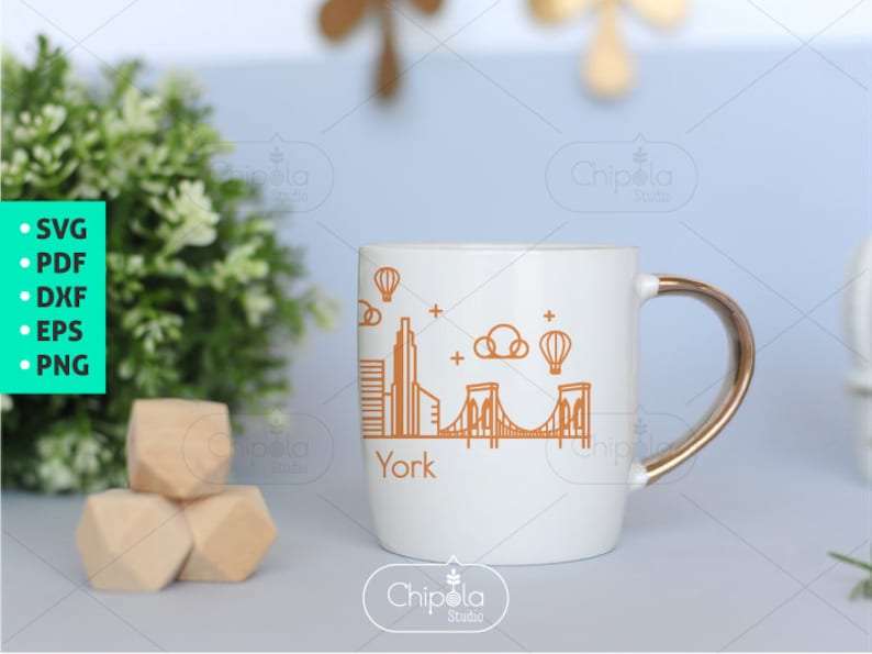 May include: White ceramic mug with a gold handle featuring a line drawing of the New York City skyline, including the Brooklyn Bridge, and the word "York" printed below the image.