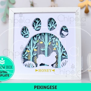 May include: A white framed shadow box with a layered design featuring a dog paw print, trees, and a Pekinese dog silhouette. The name "HONEY" is below the dog. The design includes the text "SVG, PDF, DXF, EPS, PNG" and "SHADOW BOX, DIGITAL TEMPLATE".