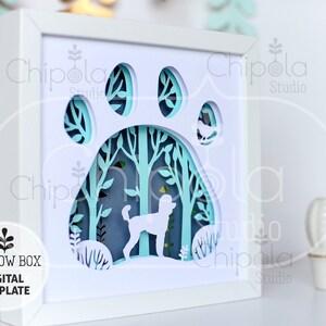 May include: A white shadow box with a paw print design, featuring a poodle silhouette within a forest scene. The layered paper art is framed in white, with the text "SHADOW BOX DIGITAL TEMPLATE" and file type icons on the left.