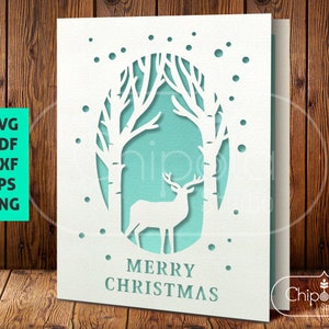 May include: A white card with a cut-out design of a deer standing in a snowy forest. The card has a light blue background and the text "Merry Christmas" in white.