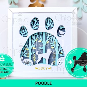 May include: A white framed shadow box featuring a poodle silhouette within a paw print design. The layered paper art includes trees and the name "LUCY". Additional graphics include a poodle silhouette and the word "POODLE".
