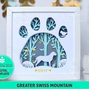May include: A white shadow box with a paw print cutout. Inside the paw print is a blue and green forest scene with a dog silhouette. The dog is labeled "GRAY". The box is labeled "GREATER SWISS MOUNTAIN".