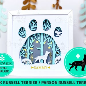 May include: A white frame with a blue paw print design inside. The paw print has a forest scene with trees and a small bird. The name "SAMMY" is written below the paw print. The frame is on a white surface with a green circle containing a black silhouette of a Jack Russell Terrier.