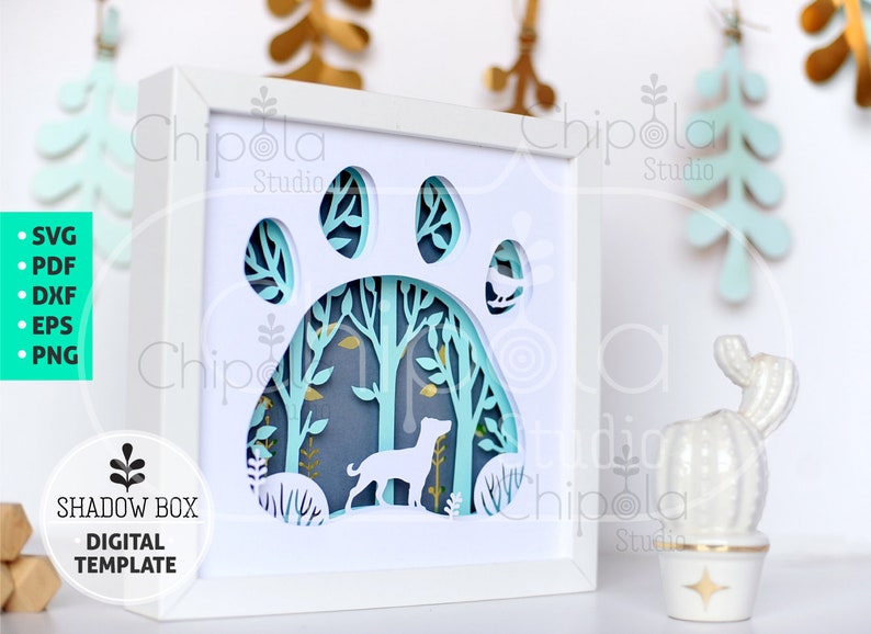 May include: A white shadow box with a paw print design. The paw print is cut out and the inside is decorated with a forest scene with a dog and birds. The text "SHADOW BOX DIGITAL TEMPLATE" is on the bottom left corner of the image.