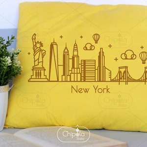 May include: A yellow pillow with a brown outline of the New York City skyline, including the Statue of Liberty, the Empire State Building, and the Brooklyn Bridge. The text "New York" is below the skyline.