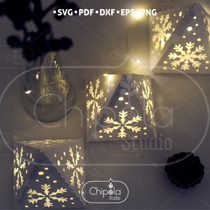May include: Four white paper snowflake lanterns with a string of fairy lights. The lanterns are illuminated from within, casting a warm glow. The lanterns are decorated with snowflakes and dots.