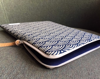 May include: A blue and white patterned laptop sleeve with a zipper closure and a brown leather strap. The sleeve is lined with a dark blue fabric.