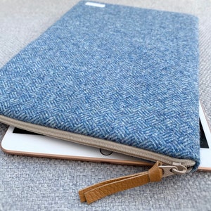 May include: A blue tweed zippered case with a brown leather pull tab, holding a tablet computer.