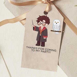May include: A tan gift tag with a cartoon illustration of a boy in a wizard robe holding a wand, and a white owl. The tag reads "THANKS FOR COMING TO MY PARTY!" and is tied with a gold ribbon.