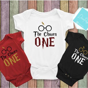 May include: Three baby onesies with the text "The Chosen One" and a graphic of Harry Potter's glasses and lightning bolt. The onesies are red, white, and black.