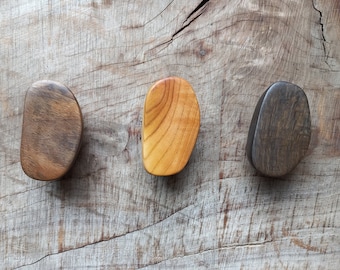 May include: Three wooden coasters in different shades of brown, with a natural wood grain pattern. The coasters are oval shaped and have a smooth, polished finish.