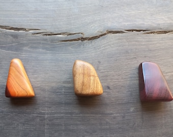 May include: Three wooden triangular shapes in different shades of brown and purple. The shapes are arranged in a row on a dark wood surface.