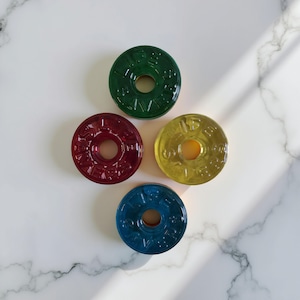 May include: Four round, colorful candy discs with a hole in the center. The candies are green, red, yellow, and blue.