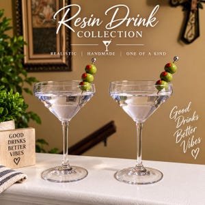 May include: Two clear glass martini glasses filled with clear resin liquid, each garnished with a metal pick holding three green olives with red pimentos. Text reads Resin Drink COLLECTION, REALISTIC, HANDMADE, ONE OF A KIND, and Good Drinks Better Vibes.