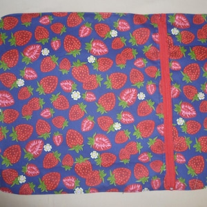 May include: A rectangular, blue fabric item patterned with red strawberries, green leaves, and white flowers. A red zip runs vertically down the right side. A green fabric loop is attached to the left side.