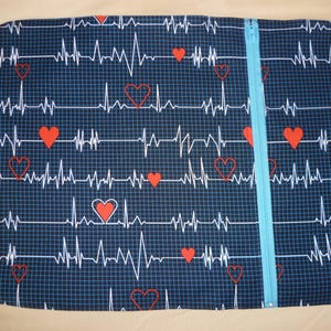 May include: A blue zippered pouch with a repeating pattern of red hearts and white EKG lines. The pouch is made of fabric and has a blue zipper.