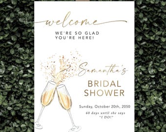 Puede incluir: Un letrero blanco sobre un caballete con letras doradas que dice "¡bienvenidos, nos alegra mucho que estén aquí!" y "Samantha's Bridal Shower". Dos copas de champán chocan, con la fecha y una cuenta regresiva.