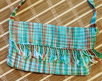May include: A green, brown and white woven crossbody bag with a fringe trim. The bag has a plaid pattern and a long strap.