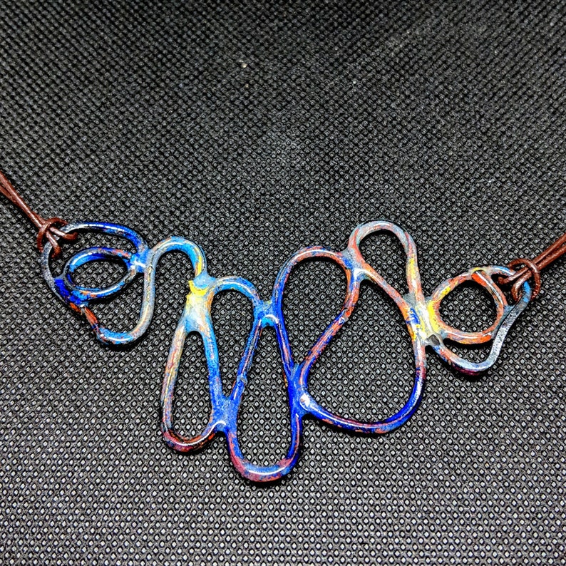 May include: A blue, red, and yellow abstract metal necklace with a brown leather cord.