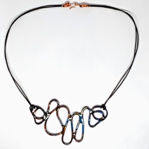 May include: A necklace with a long black cord and a multi-colored metal pendant. The pendant is made of several interconnected loops of metal, with a blue, gold, and copper finish.