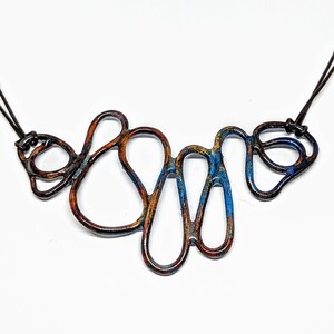 May include: A copper necklace with a blue and orange patina. The necklace is made of a series of interconnected loops and is designed to be worn as a statement piece.