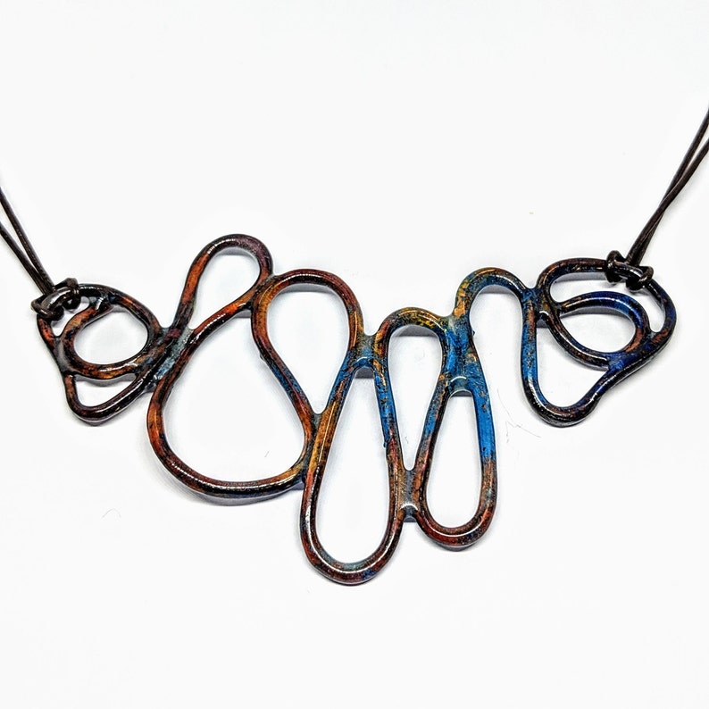 May include: A copper necklace with a blue and orange patina. The necklace is made of a series of interconnected loops and is designed to be worn as a statement piece.
