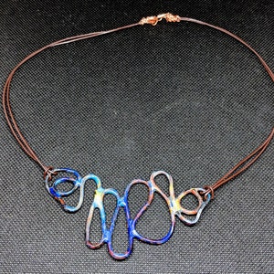 May include: A blue, yellow, and brown abstract metal necklace with a brown leather cord.