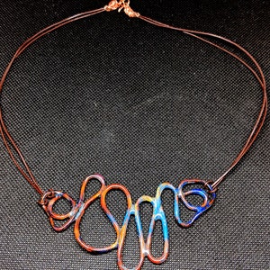 May include: A copper wire necklace with a blue, orange, and yellow enamel design. The necklace is made of multiple loops and curves.