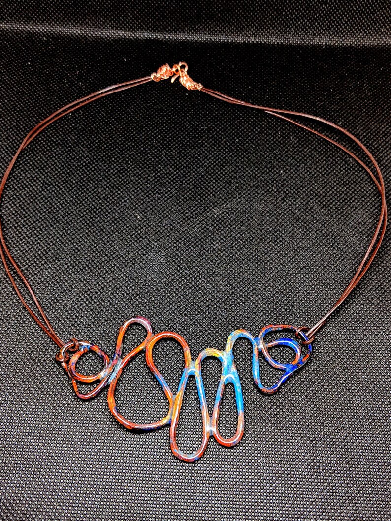May include: A copper wire necklace with a blue, orange, and yellow enamel design. The necklace is made of multiple loops and curves.