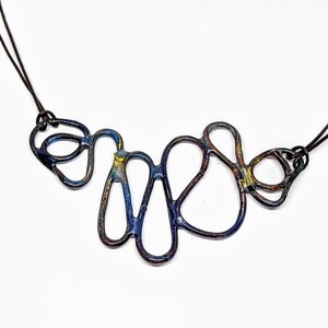 May include: A blue, yellow, and brown abstract metal necklace with a leather cord. The necklace is made of interconnected loops and curves.