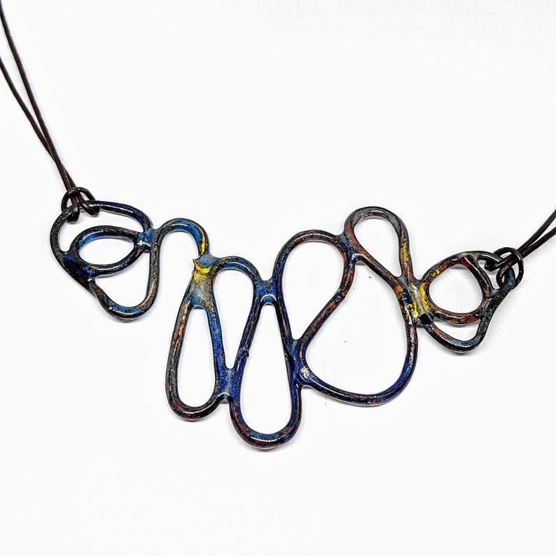 May include: A blue, yellow, and brown abstract metal necklace with a leather cord. The necklace is made of interconnected loops and curves.