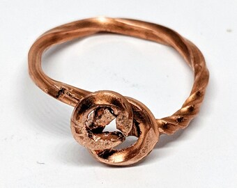 May include: A copper ring with a twisted band and a knot design. The knot is a simple, rounded shape with a hole in the centre.
