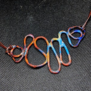 May include: A copper wire necklace with a blue and orange enamel finish. The wire is shaped into a series of abstract loops and curves.