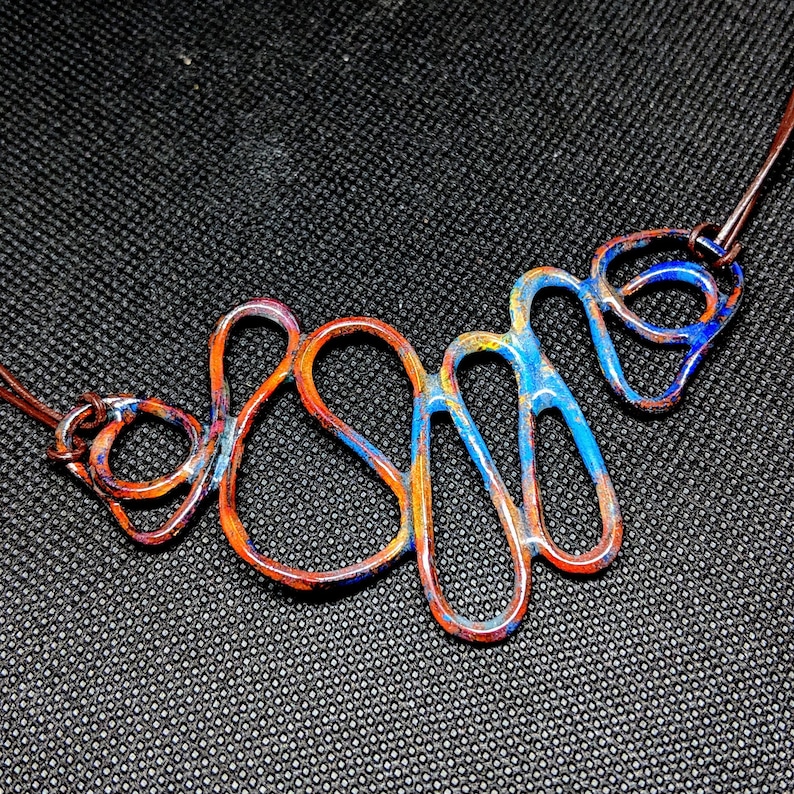 May include: A copper wire necklace with a blue and orange enamel finish. The wire is shaped into a series of abstract loops and curves.