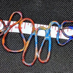 May include: A colorful copper wire necklace with blue, orange, and yellow enamel paint. The necklace is approximately 3 inches long and is measured with a tape measure.