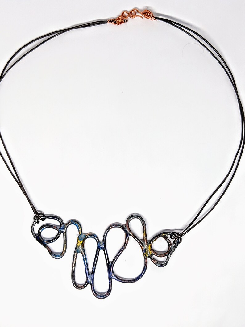 May include: A black necklace with a copper clasp and a blue and yellow abstract metal pendant.