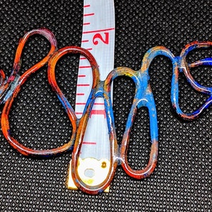 May include: A copper wire necklace with blue and orange enamel paint. The necklace is about 2 inches long and has a unique, abstract design.