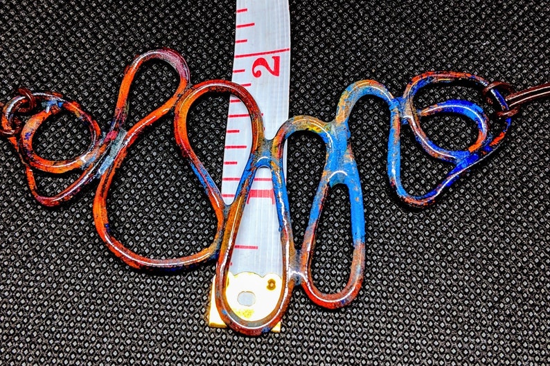 May include: A copper wire necklace with blue and orange enamel paint. The necklace is about 2 inches long and has a unique, abstract design.