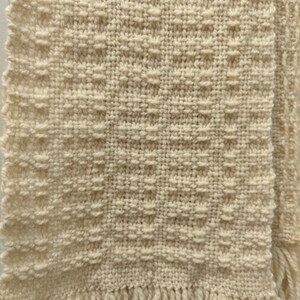 May include: A cream-coloured woven scarf with a textured pattern and fringe on the ends.