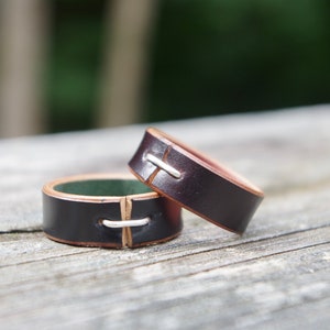 May include: Two brown leather rings with silver stitching. The rings are stacked on top of each other.