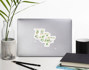 May include: A laptop computer with a sticker on it. The sticker is white with a green, blue, and yellow floral pattern. The sticker says "WLF" in a stylized font.