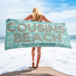 May include: A turquoise beach towel with a white seashell pattern. The text "COUSINS BEACH NORTH CAROLINA" is printed in brown on the towel.