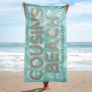 May include: A turquoise beach towel with a white seashell pattern and the text "COUSINS BEACH - NORTH CAROLINA" in brown lettering.